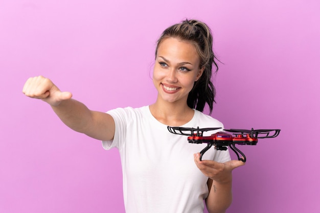 Teenager Russian girl holding a drone isolated on purple background giving a thumbs up gesture