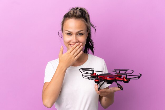 Adolescente ragazza russa in possesso di un drone isolato su sfondo viola felice e sorridente che copre la bocca con la mano Foto Premium