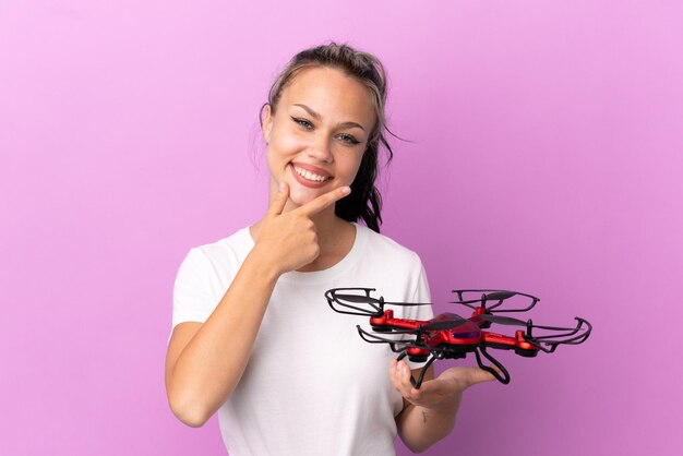 Teenager Russian girl holding a drone isolated on purple background happy and smiling