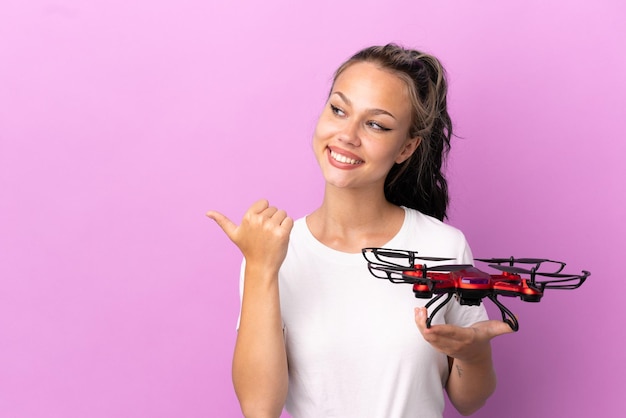 Teenager Russian girl holding a drone isolated on purple background pointing to the side to present a product