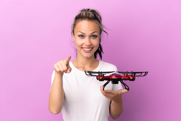 Teenager Russian girl holding a drone isolated on purple background surprised and pointing front