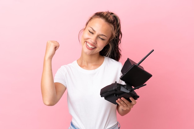 Teenager Russian girl holding a drone remote control isolated on pink background celebrating a victory