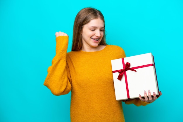 Teenager Russian girl holding a gift isolated on blue background celebrating a victory