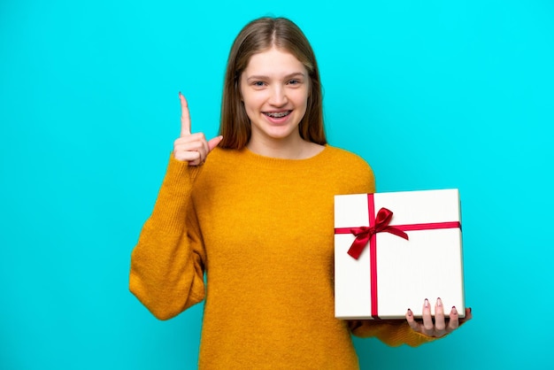 素晴らしいアイデアを指している青い背景に分離された贈り物を保持している 10 代のロシアの女の子