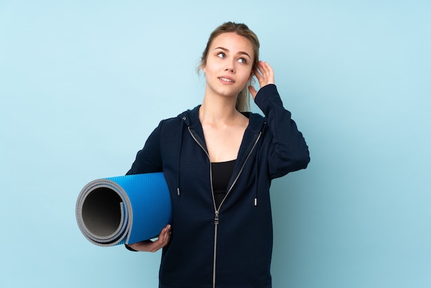 Teenager Russian girl holding mat isolated on blue thinking an idea