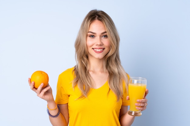 Teenager Russian girl holding an orange isolated on blue