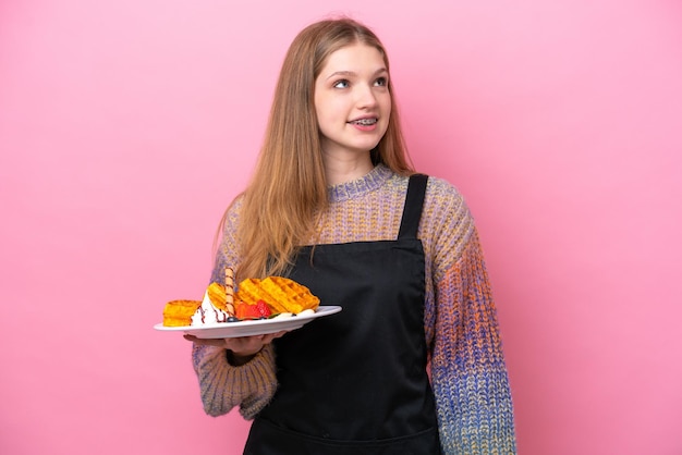 Teenager Russian girl holding a waffles isolated on pink background thinking an idea while looking up