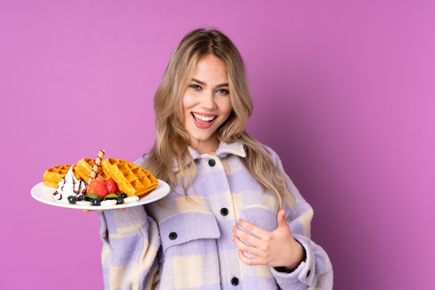 Photo teenager russian girl holding waffles isolated on purple