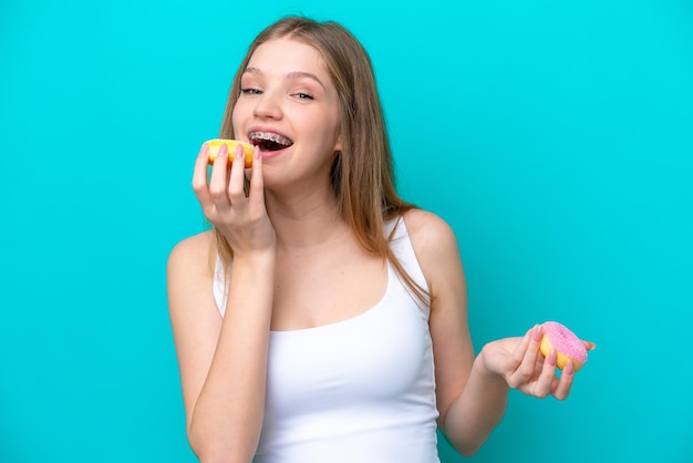 Teenager Russian girl isolated on blue background eating a donut