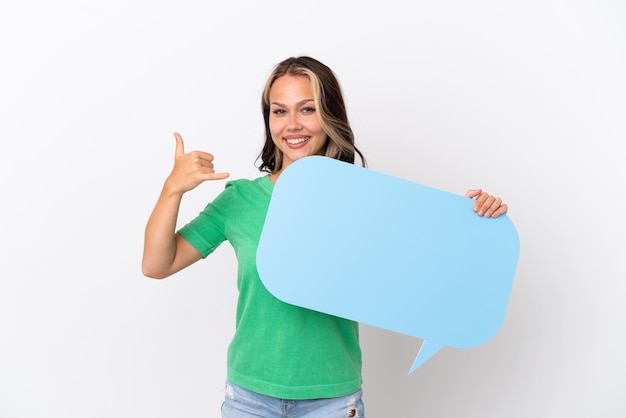 Teenager Russian girl isolated on blue background holding an empty speech bubble and doing phone gesture