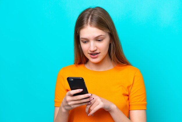 Teenager Russian girl isolated on blue background sending a message or email with the mobile