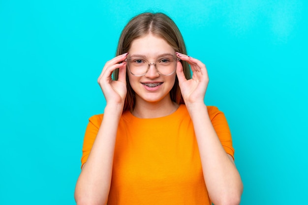 Teenager russian girl isolated on blue background with glasses with happy expression