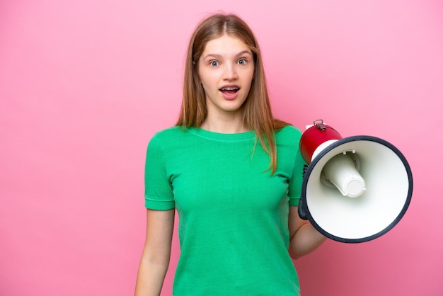 Teenager Russian girl isolated on pink background holding a megaphone and with surprise expression