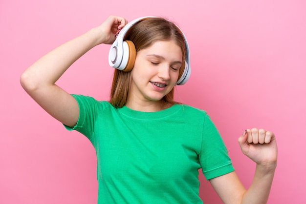 Русская девушка-подросток изолирована на розовом фоне, слушает музыку и танцует