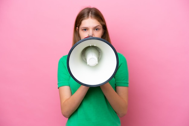 Teenager Russian girl isolated on pink background shouting through a megaphone to announce something