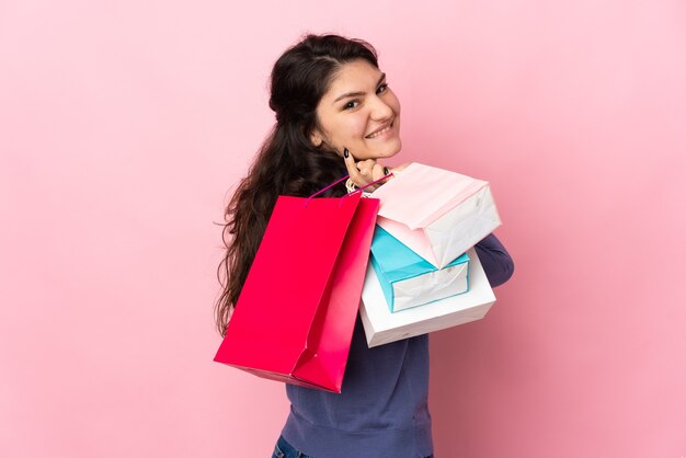 Teenager Russian girl isolated on pink wall holding shopping bags and smiling