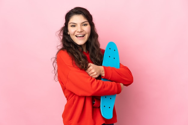 Teenager Russian girl isolated on pink wall with a skate with happy expression