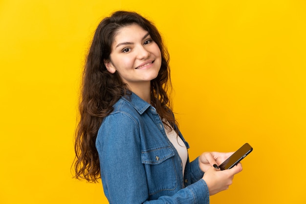 Teenager Russian girl isolated on yellow wall sending a message or email with the mobile