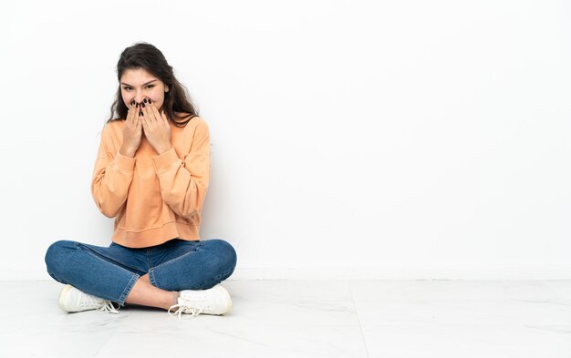 Ragazza russa dell'adolescente che si siede sul pavimento felice e sorridente che copre la bocca con le mani