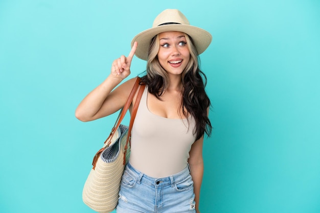 Teenager Russian girl with pamel and beach bag isolated on blue background intending to realizes the solution while lifting a finger up