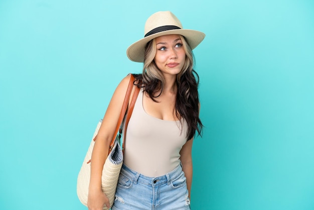 Teenager Russian girl with pamel and beach bag isolated on blue background and looking up