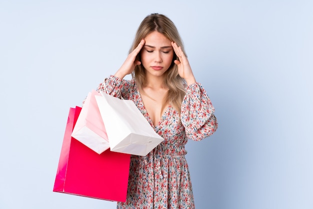 Teenager Russian girl with shopping bag isolated on blue wall with headache