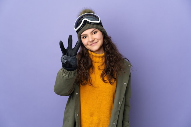 Teenager Russian girl with snowboarding glasses isolated on purple wall happy and counting three with fingers