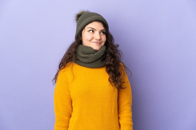 Teenager Russian girl with winter hat isolated on purple background thinking an idea while looking up