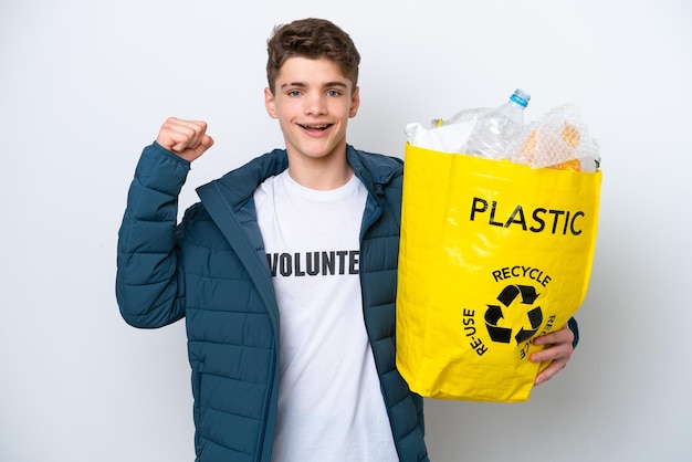 Teenager Russian holding a bag full of plastic bottles to recycle on white background celebrating a victory