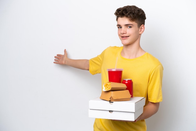 Adolescente uomo russo che tiene fast food isolato su sfondo bianco estendendo le mani di lato per invitare a venire