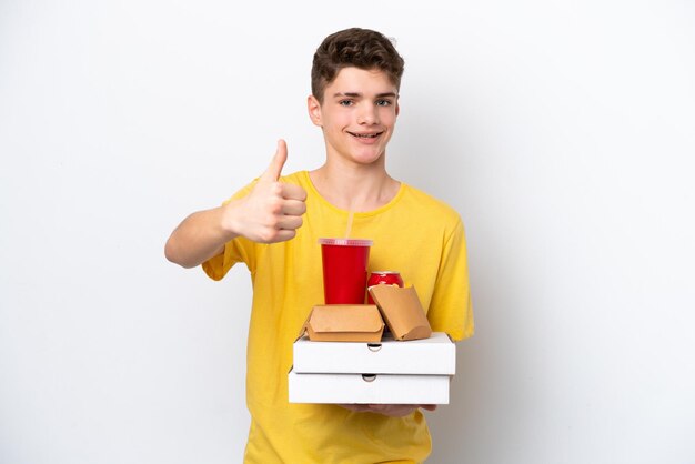 Teenager Russian man holding fast food isolated on white background with thumbs up because something good has happened