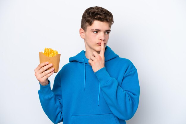 Teenager Russian man holding fried potatoes isolated on white background having doubts while looking up