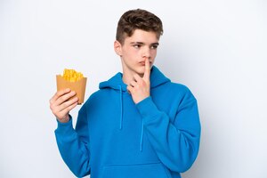 Teenager russian man holding fried potatoes isolated on white background having doubts while looking up