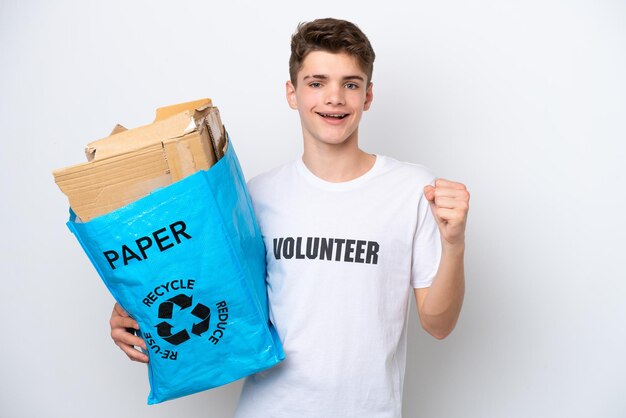 Teenager Russian man holding a recycling bag full of paper to recycle isolated on white background celebrating a victory in winner position