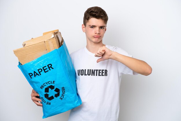 Teenager russian man holding a recycling bag full of paper to\
recycle isolated on white background showing thumb down with\
negative expression