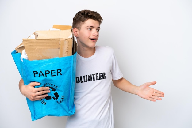 Подросток русский мужчина держит мешок для переработки, полный бумаги для переработки, изолированный на белом фоне с удивленным выражением лица, глядя в сторону
