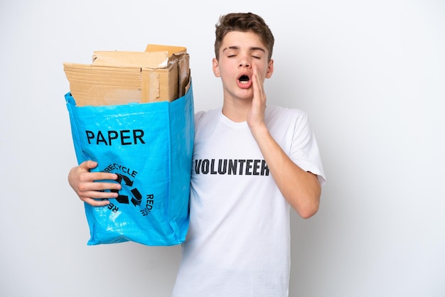 Подросток русский мужчина держит мешок для вторичной переработки, полный бумаги для переработки, изолированный на белом фоне с удивленным и шокированным выражением лица