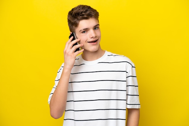 Teenager Russian man isolated on yellow background keeping a conversation with the mobile phone with someone