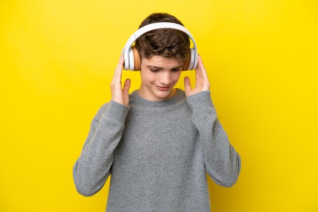 Teenager Russian man isolated on yellow background listening music