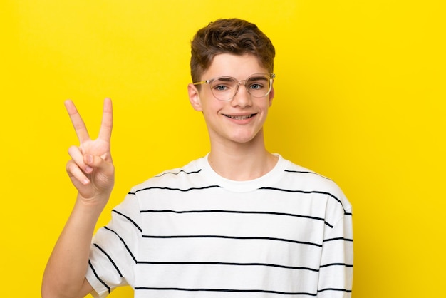 Подросток русский мужчина изолирован на желтом фоне в очках и делает знак ОК