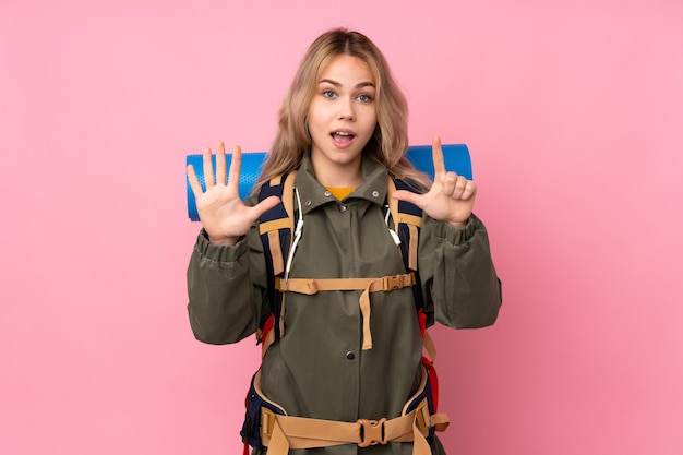 指で7を数えるピンクの壁に分離された大きなバックパックを持つ10代のロシアの登山家の女の子