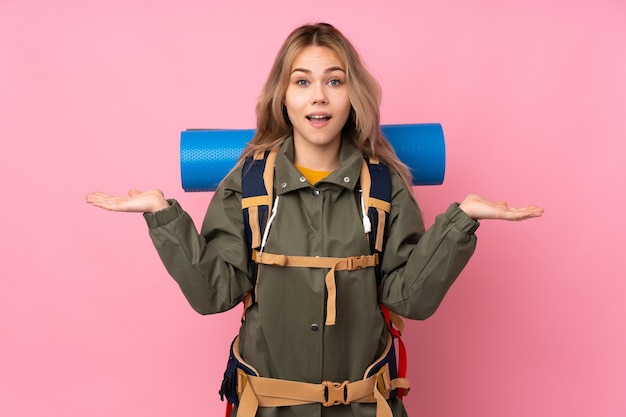 Ragazza russa dell'alpinista dell'adolescente con un grande zaino isolato sul colore rosa con l'espressione facciale scioccata