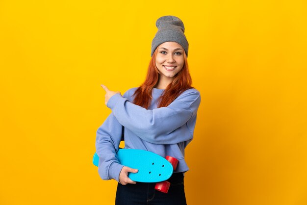 Teenager Russian skater girl isolated on yellow wall pointing back