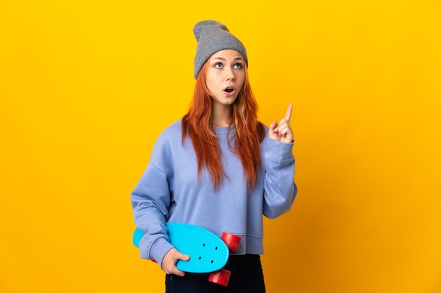 Photo teenager russian skater girl isolated on yellow wall thinking an idea pointing the finger up