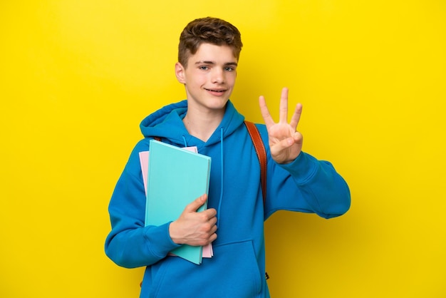 Teenager Russian student man isolated on yellow background happy and counting three with fingers