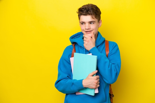 横を見て笑っている黄色の背景に分離された10代のロシアの学生の男