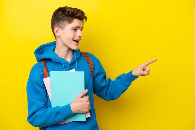 Подросток русский студент мужчина изолирован на желтом фоне, указывая пальцем в сторону и представляя продукт