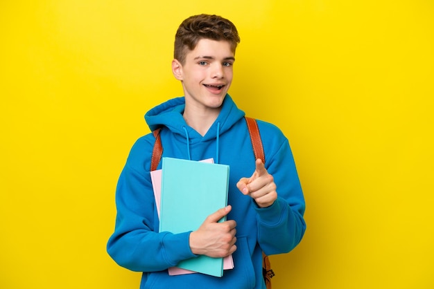 黄色の背景に分離されたティーンエイジャーのロシアの学生の男は驚いて正面を指しています