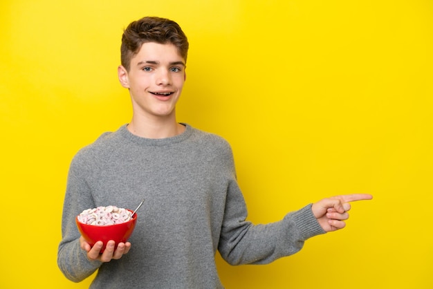 Teenager Russian woman holding a yellow background surprised and pointing finger to the side