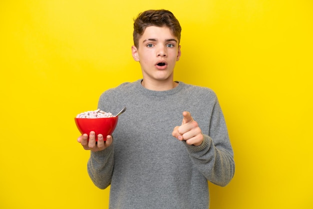 Teenager Russian woman holding a yellow background surprised and pointing front